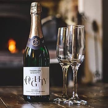 A bottle of sparkling wine with two flutes set on a wooden table by a fireplace