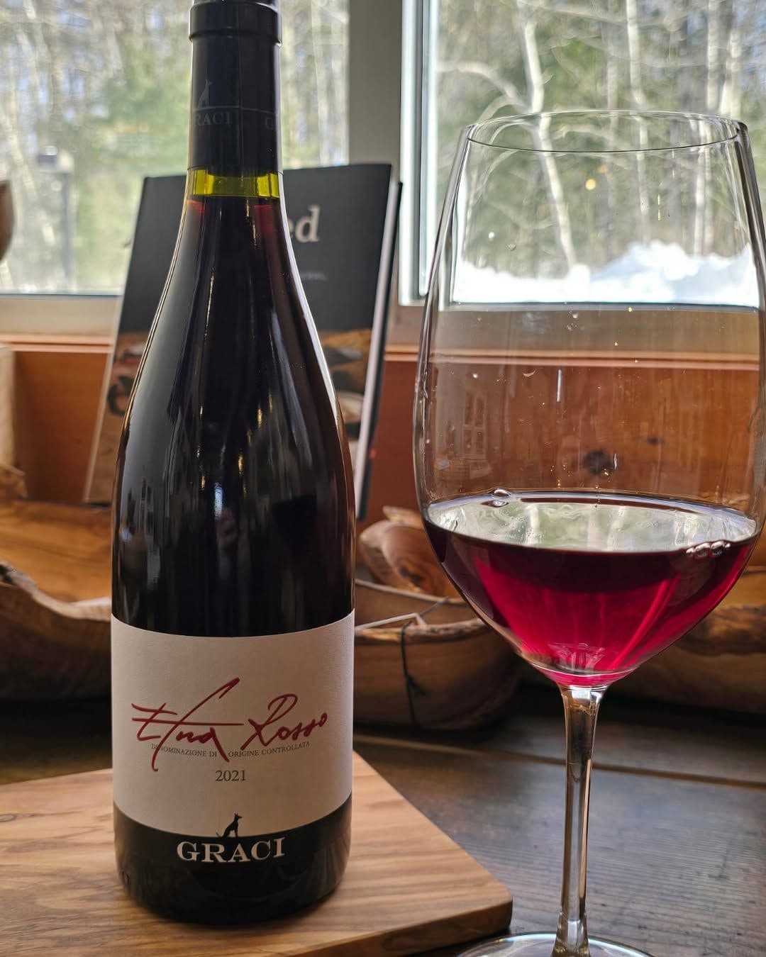A bottle of Graci Etna Rosso 2021 with a poured glass on a wooden counter at The Clown